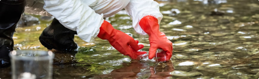 A water quality technician wearing safety gloves collects a sample of surface water.