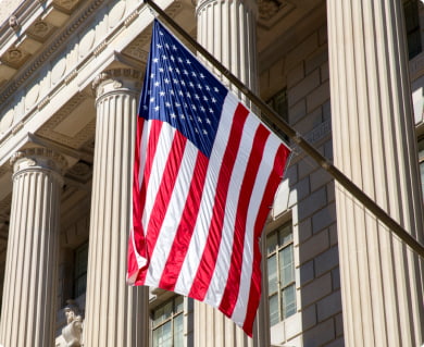 Closeup of the American flag hanging outside a stately government building with ornate columns.