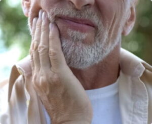 Closeup of a man grimacing and clutching his cheek, indicating dental pain.
