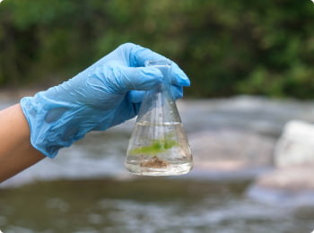 A close-up of a hand in a rubber glove holding a glass tube filled with water from a freshwater source.