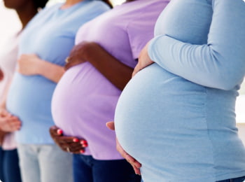 Four pregnant women standing side by side, each holding their belly.
